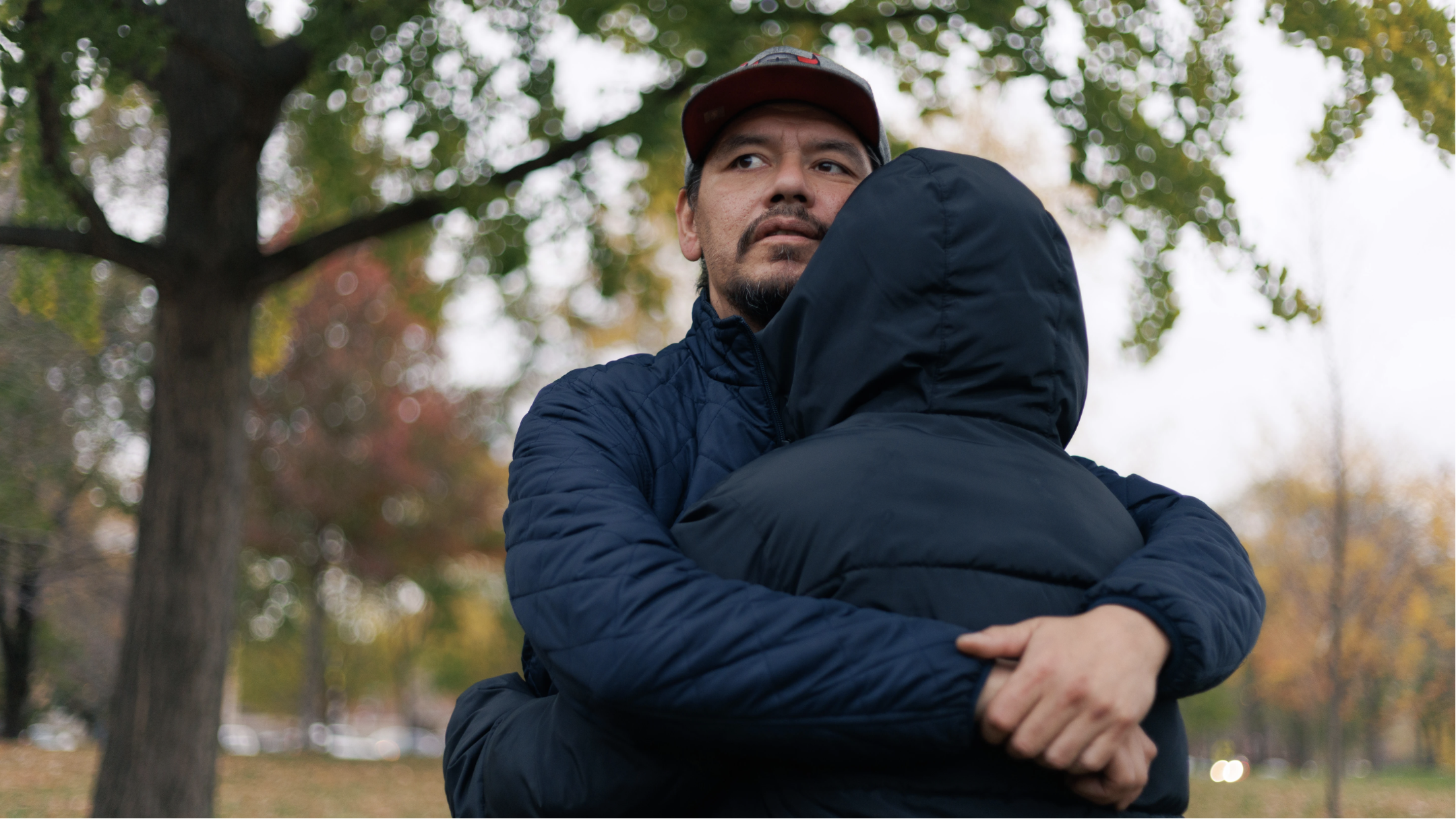 A man embraces another person. They are standing outside wearing coats.